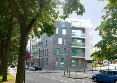 Immeuble d'angle finalisé par Dawo Group, façade en briques grises avec balcons vitrés, vu depuis une avenue arborée