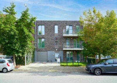 Vue de face d'un immeuble à appartements finalisé par Dawo Group, entre deux arbres, avec jardinet et entrée de garage